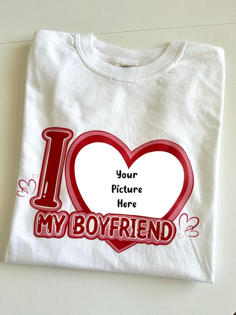 May include: White t-shirt with a red and pink heart design. The shirt features the text "I MY BOYFRIEND" with a space in the heart for a picture. Small heart graphics are on the sides.