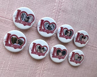 May include: A collection of white round buttons with a red heart design and the text "I MY BOYFRIEND". Each button features a photograph inside the heart. The buttons are arranged on a pink surface.