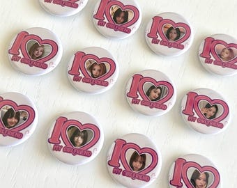 May include: A collection of white round buttons with a pink heart and the text "I MY GIRLFRIEND". Each button features a photo of a person inside the heart. The buttons are scattered on a white surface.