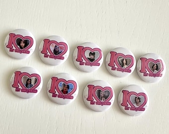 May include: A collection of ten white round buttons. Each button features a pink heart with a photo inside and the text "I MY GIRLFRIEND" in pink. The buttons are arranged on a light-colored surface.