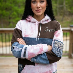 May include: A hooded sweatshirt with a unique design. The top portion is brown and white tie-dye, with a denim blue section across the chest and denim sleeves. The text "I walk with Jesus" is written on the upper right chest.