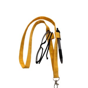 May include: A yellow lanyard with a black pen and black-framed reading glasses attached. The lanyard has a metal clasp and a loop for wearing around the neck. The pen is black and the glasses are folded.