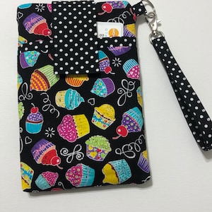 May include: Black fabric phone case with a colorful cupcake pattern and a black and white polka dot flap. The case has a black and white polka dot wrist strap.