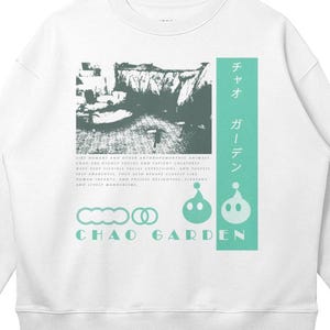 Puede incluir: Sudadera blanca de cuello redondo con un diseño gráfico. El diseño presenta una imagen de paisaje en blanco y negro, texto japonés y las palabras "CHAO GARDEN" en color turquesa. La sudadera tiene mangas largas y un corte holgado.