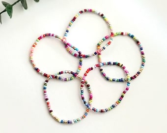 May include: A set of four colorful beaded bracelets with a mix of bright colors, including pink, blue, green, yellow, and purple. The bracelets are made with small, round beads and are strung on a thin, silver-colored thread.