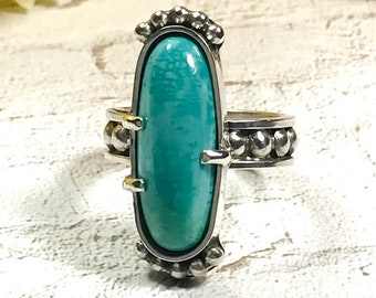 May include: A silver ring with a turquoise stone set in a bezel setting. The ring has a beaded band.