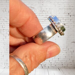 Puede incluir: Un anillo de plata con una banda texturizada y un detalle de cuentas en la parte superior. El anillo se lleva en un dedo.