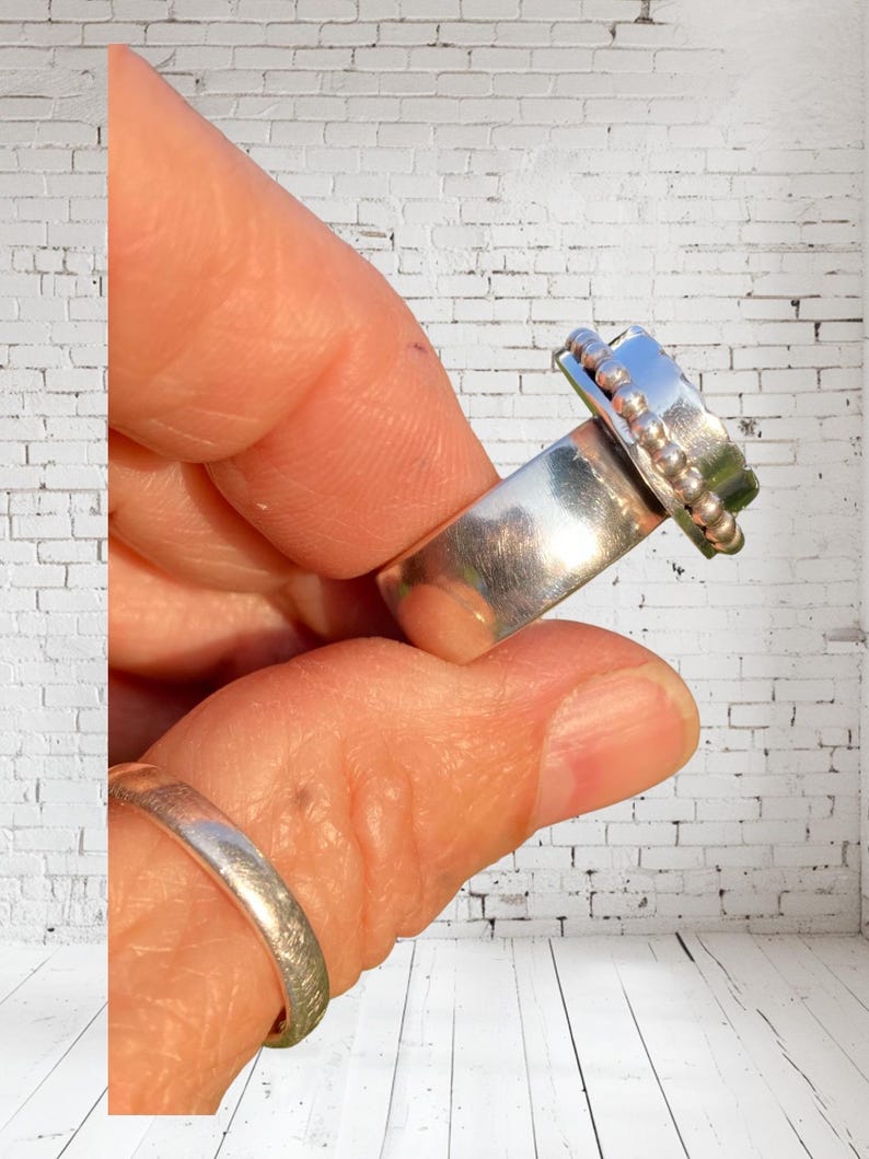 Puede incluir: Un anillo de plata con una banda texturizada y un detalle de cuentas en la parte superior. El anillo se lleva en un dedo.