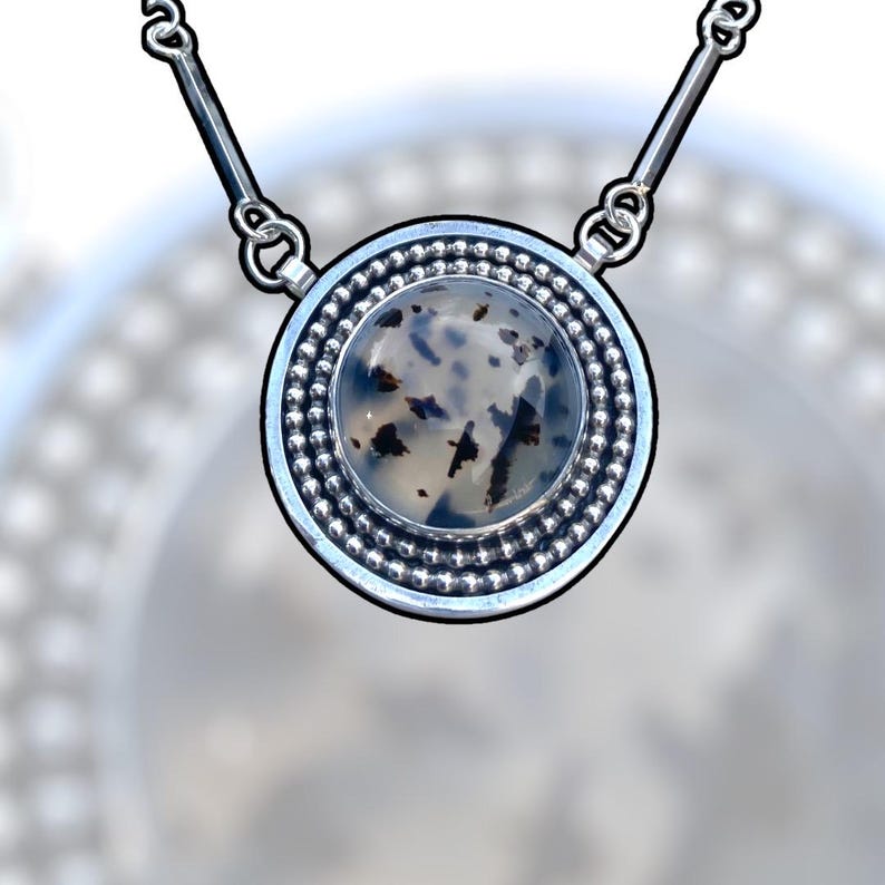 May include: A silver pendant necklace featuring a round, speckled stone. The stone is encased in a silver bezel with a beaded border. The necklace has a simple, elegant design, suitable for everyday wear.