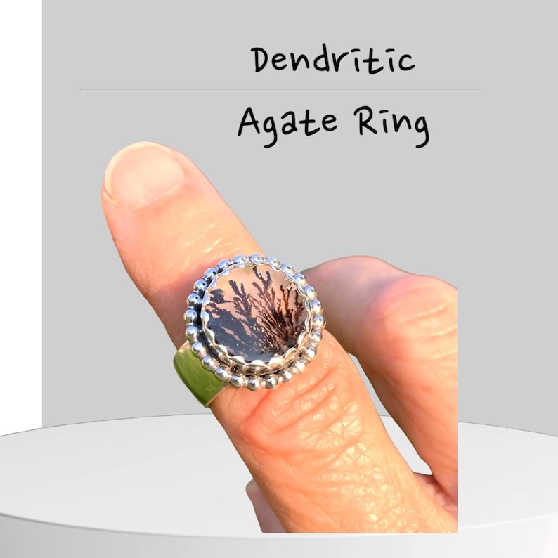Puede incluir: Un anillo de plata con una piedra redonda de &aacute;gata dendr&iacute;tica engastada en un engaste de cuentas. El &aacute;gata tiene un fondo blanco transl&uacute;cido con patrones dendr&iacute;ticos negros.