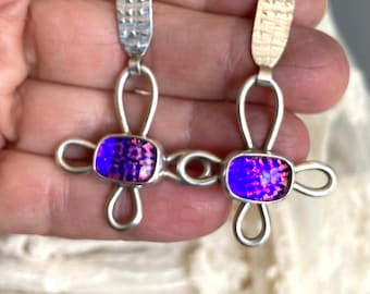 Può includere: Un paio di orecchini d'argento con un design in vetro viola e rosa. Gli orecchini hanno una barra d'argento testurizzata nella parte superiore e un design ad anello.