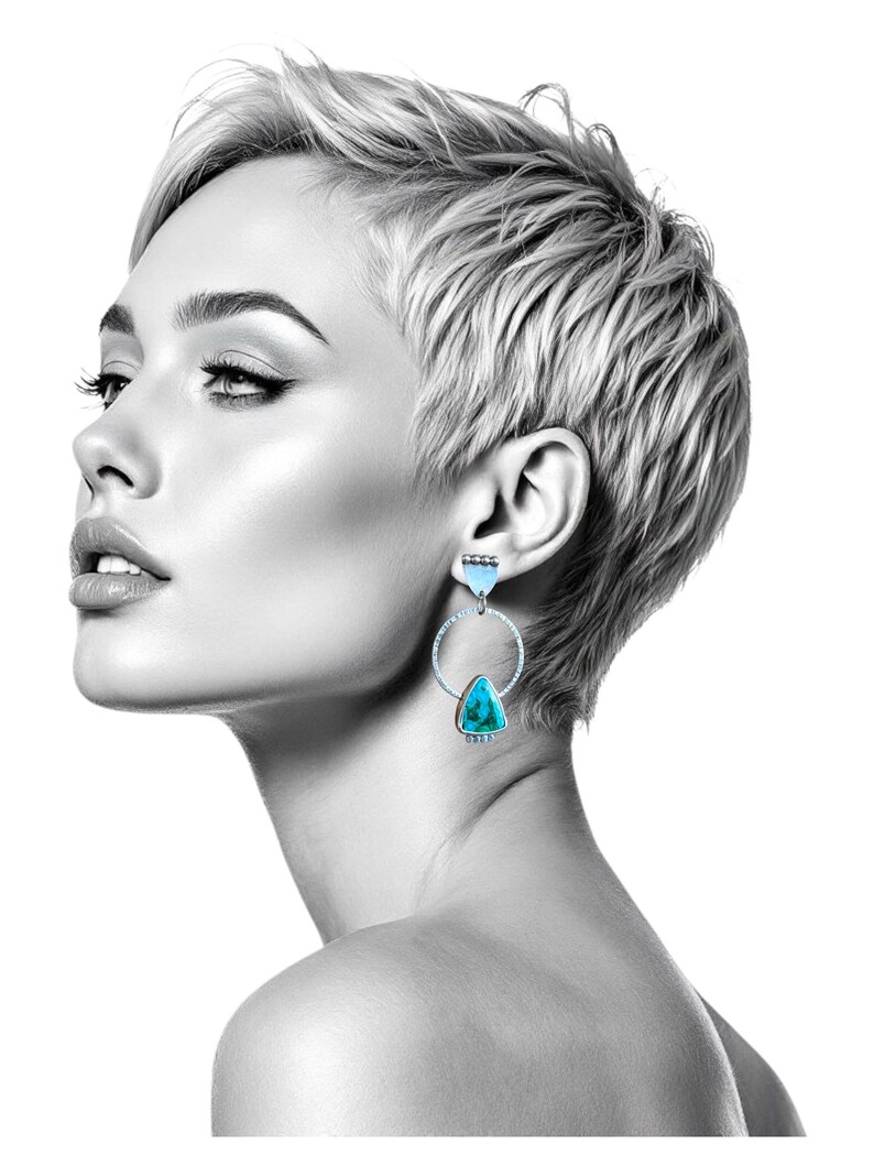 May include: A black and white image of a person wearing turquoise and silver earrings. The earrings feature a triangular turquoise stone suspended within a silver hoop. The person has short, light-colored hair and is looking to the side.