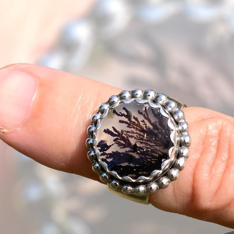 Puede incluir: Un anillo de plata con una piedra redonda de &aacute;gata dendr&iacute;tica negra y blanca engastada en un engaste de cuentas.