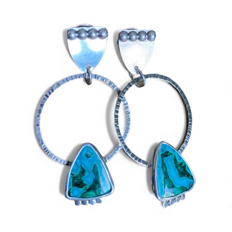 May include: A pair of silver earrings with a textured hoop design. Each earring features a turquoise and green triangular stone pendant. The earrings have a silver shield-shaped top with small silver beads.