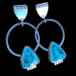 May include: A pair of silver earrings with a textured hoop design. Each earring features a triangular turquoise stone with a silver border, and a silver top with a row of small silver beads. The earrings hang from a silver post.