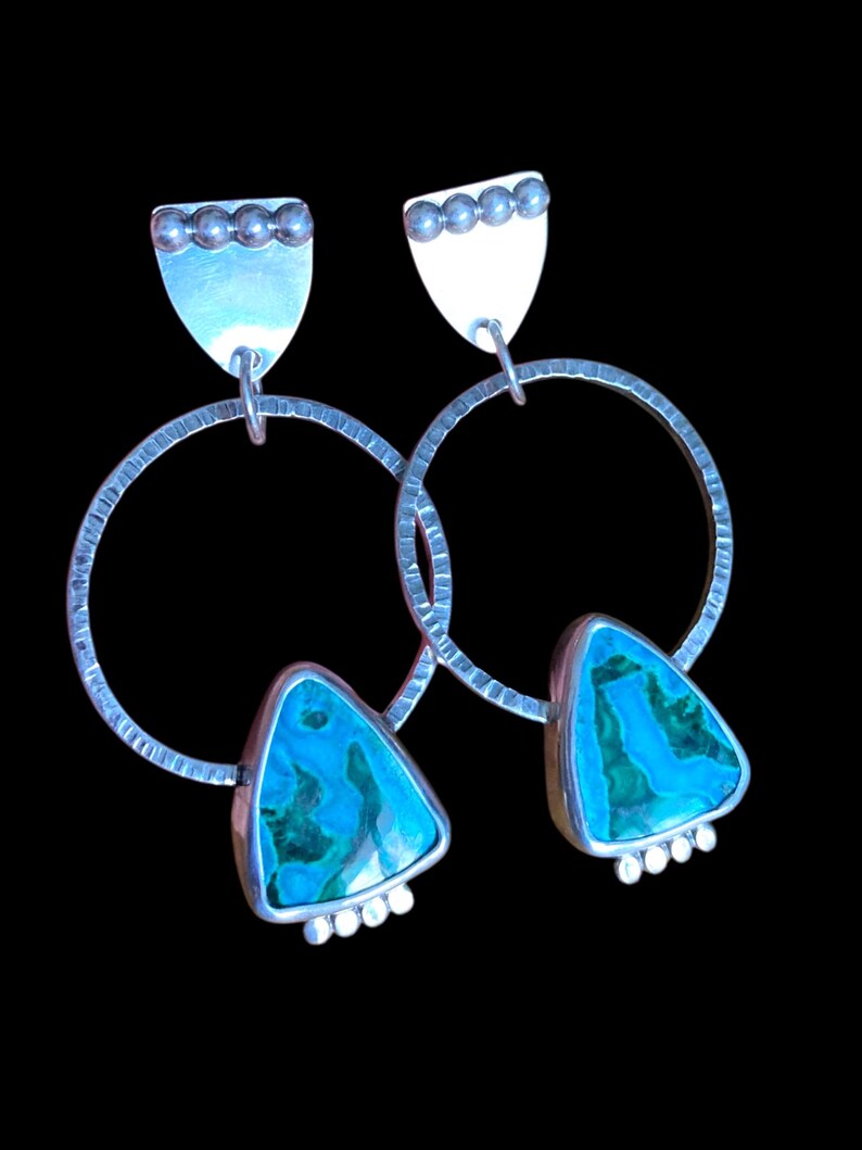 May include: A pair of silver earrings with a textured hoop design. Each earring features a triangular turquoise stone with a silver border, and a silver top with a row of small silver beads. The earrings hang from a silver post.