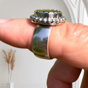 Puede incluir: Un anillo de plata con una parte superior redonda de color dorado. La parte superior tiene un borde de cuentas y una superficie texturizada.