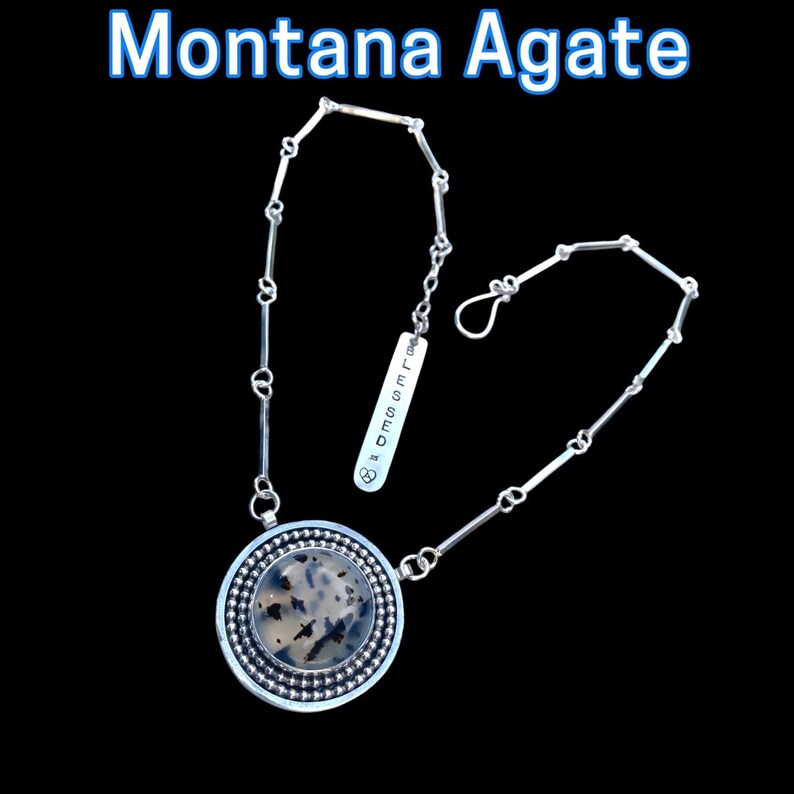 May include: A silver necklace with a round pendant featuring a Montana Agate stone with black and white patterns. The necklace has a chain design and a small tag that reads "Blessed". The text "Montana Agate" is at the top.