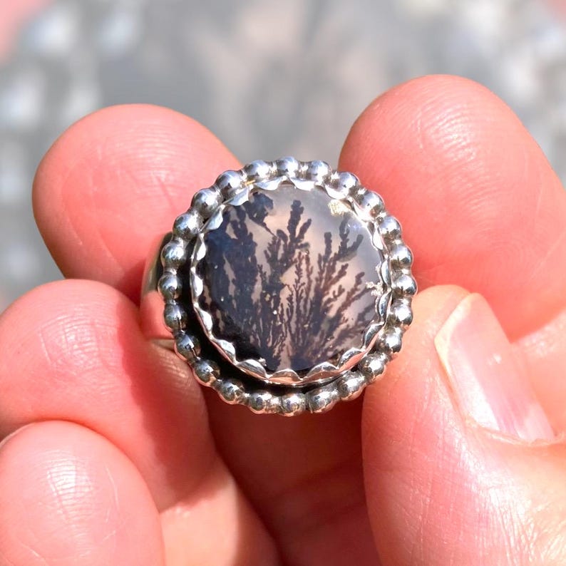 Puede incluir: Un anillo de plata con una piedra redonda de &aacute;gata dendr&iacute;tica engastada en un engaste de cuentas. La piedra tiene un patr&oacute;n dendr&iacute;tico negro y blanco.