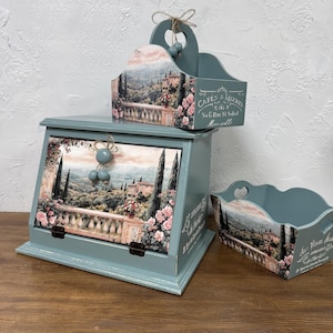 Könnte beinhalten: Ein Set aus drei dekorativen Aufbewahrungsboxen aus Holz in einem gedämpften Türkis. Jede Box zeigt ein Landschaftsdesign mit Balkon, Blumen und Gebäuden. Eine Box hat einen Griff und den Text "CAFES & LEGUMES".