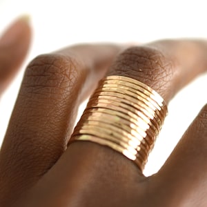 Könnte beinhalten: Ein Stapel dünner goldener Ringe, die an einem Finger getragen werden. Die Ringe sind gehämmert und haben eine strukturierte Oberfläche.