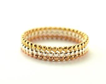 May include: Three gold rings stacked on top of each other. The top ring is yellow gold, the middle ring is white gold, and the bottom ring is rose gold. Each ring is made of small, round beads.
