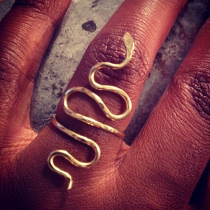 Puede incluir: Un anillo de serpiente de oro con un acabado texturizado. El anillo se lleva en un dedo.