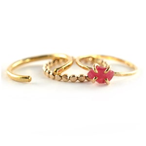 Op de afbeelding: Set van drie gouden ringen, &eacute;&eacute;n met een roze edelsteen, &eacute;&eacute;n met een kralenband en &eacute;&eacute;n met een eenvoudige band.