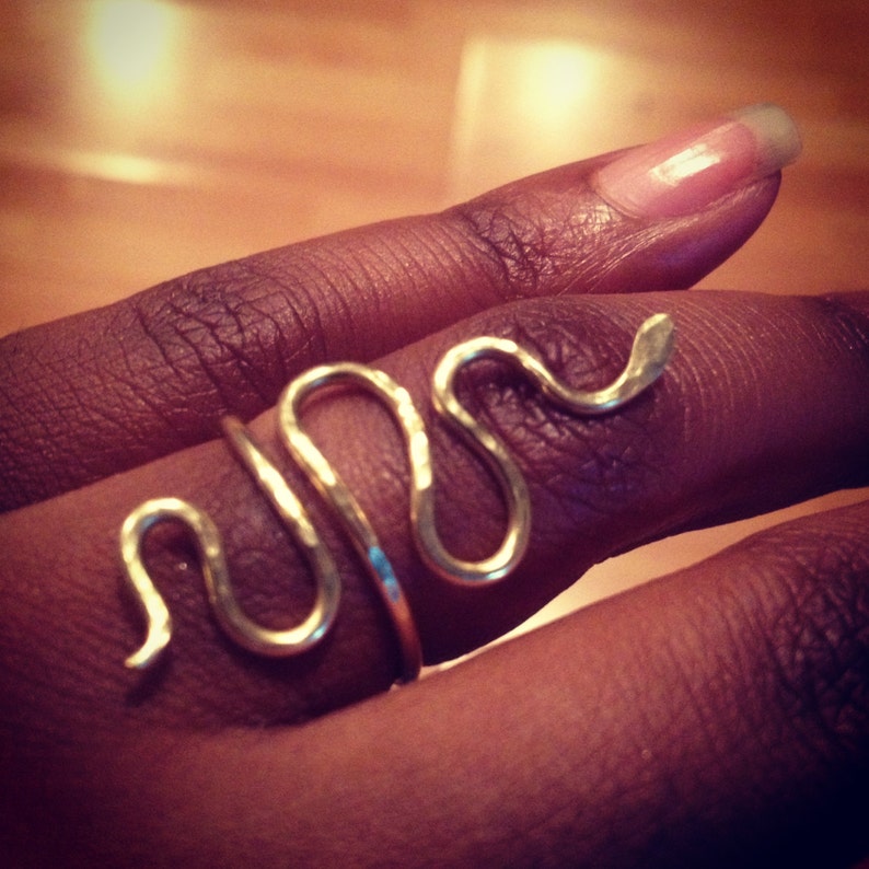 Puede incluir: Un anillo de serpiente de oro con un acabado texturizado. El anillo se lleva en un dedo.