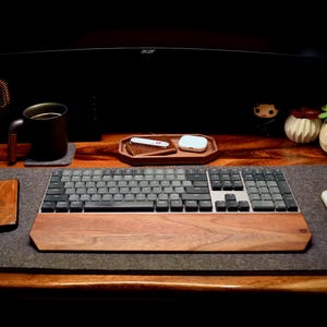 May include: A well-lit desk setup featuring a wooden keyboard with a matching wrist rest, a gray mouse pad, and a wireless mouse. A wooden phone case, a mug, and a tray with accessories are also visible.