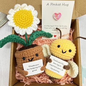 Peut inclure: Un coffret cadeau crocheté comprenant une marguerite jaune et blanche, un pot de fleur souriant et une abeille souriante, chacun tenant une petite pancarte. L'ensemble comprend une carte "A Pocket Hug" avec une épingle en forme de cœur.