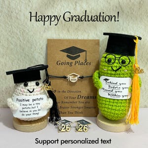Puede incluir: Una exhibición con temática de graduación con figuras de ganchillo, una pulsera y alfileres. Las figuras son una patata y una judía verde, cada una con un birrete. El texto incluye "Happy Graduation!" y mensajes inspiradores.
