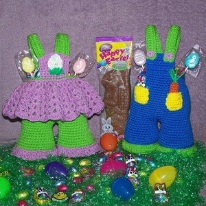 May include: Two crocheted Easter bunny figures, one in purple and green, the other in blue and green, with candy and chocolate in the background.  The text on the chocolate bar reads "Happy Easter!"