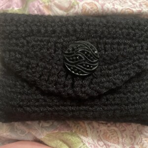May include: A black crocheted clutch with a black button closure. The button has a decorative design.