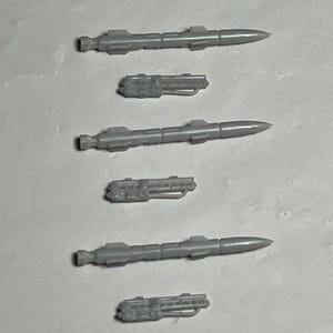 May include: Five gray plastic model missiles with fins and a pointed nose. The missiles are arranged vertically in a row, with the largest missile at the top and the smallest missile at the bottom.