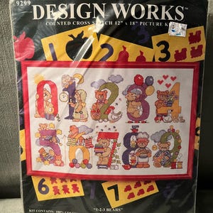 Peut inclure: Kit de point de croix compté Design Works avec les chiffres 0 à 9, chacun décoré d'un ours en peluche. Le kit comprend une toile Aida de 30,48 cm x 45,72 cm, du fil à broder et des instructions. Le motif s'intitule "1-2-3 Bears".