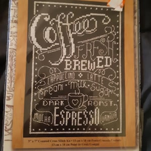 Peut inclure: Un kit de point de croix avec un motif noir et blanc, avec les mots "Coffee, Fresh Brewed, Espresso" et des termes liés au café. Le kit mesure 13 cm x 18 cm et comprend tissu, fil, aiguille et instructions.
