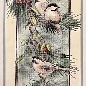 May include: Cross-stitch artwork depicting three small birds on a branch with pine needles, berries, and a pinecone. The birds have black and white markings. The background is a light blue and the artwork is framed.