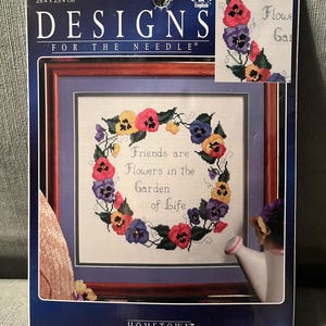 May include: A cross-stitch kit with a floral design and the text "Friends are Flowers in the Garden of Life." The kit includes a framed piece with a pansy wreath, measuring 25.4 cm x 25.4 cm. The kit is from Hometown.