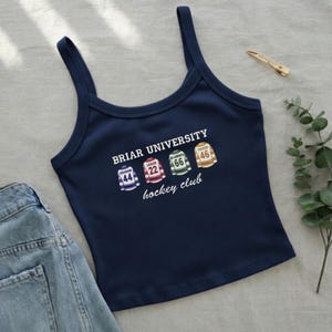 以下が含まれることがあります： ネイビーブルーのタンクトップ。前面には「Briar University hockey club」の文字と、番号と名前が入った4つのジャージのデザインが施されています。左下にはデニムのジーンズが見えます。