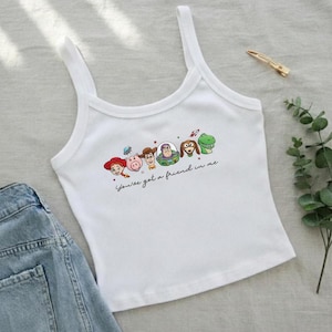 Peut inclure: D&eacute;bardeur blanc c&ocirc;tel&eacute; avec un graphisme color&eacute; des personnages de Toy Story. La phrase "You've got a friend in me" est &eacute;crite en dessous des personnages. Le d&eacute;bardeur est associ&eacute; &agrave; un short en jean.