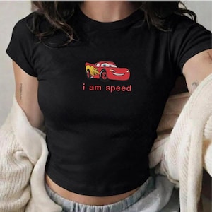 May include: Black crop top featuring a cartoon image of a red race car with the number 95 and the words "i am speed" in red. The shirt has short sleeves and a round neckline.