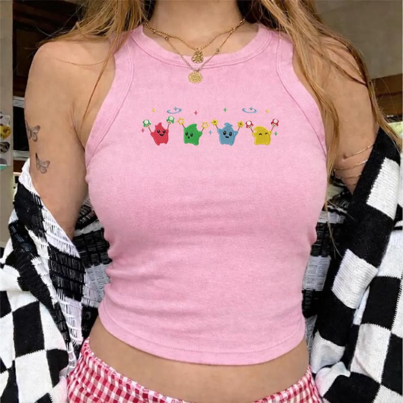 Peut inclure: D&eacute;bardeur rose clair avec un col rond et un motif color&eacute; de quatre personnages de dessins anim&eacute;s. Les personnages sont rouges, verts, bleus et jaunes, chacun tenant une &eacute;toile et un champignon. Le haut est sans manches.