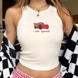 May include: White tank top with a red cartoon car graphic and the text "i am speed". The car is red with yellow accents. The top is a racerback style.