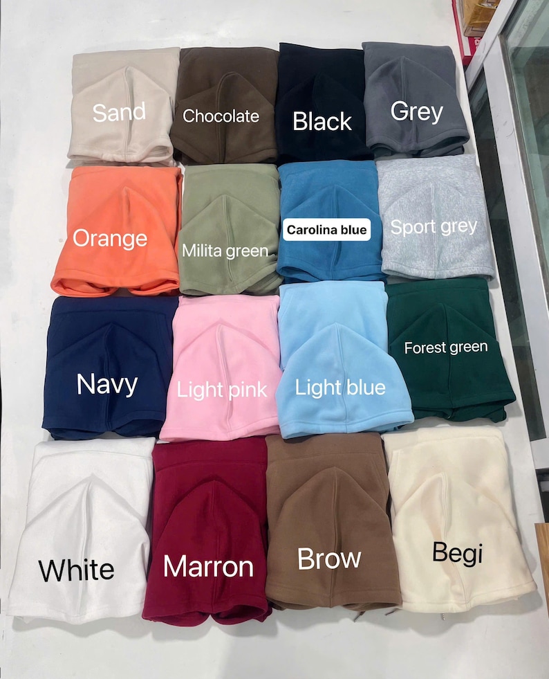 May include: A collection of fleece balaclavas in various colors, including sand, chocolate, black, grey, orange, milita green, carolina blue, sport grey, navy, light pink, light blue, forest green, white, marron, brow, and begi. Each balaclava is labeled with its color.