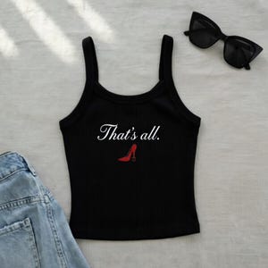 May include: Black ribbed tank top with the text "That's all." in white script and a red high heel graphic. A pair of black sunglasses and a portion of blue denim jeans are also visible.