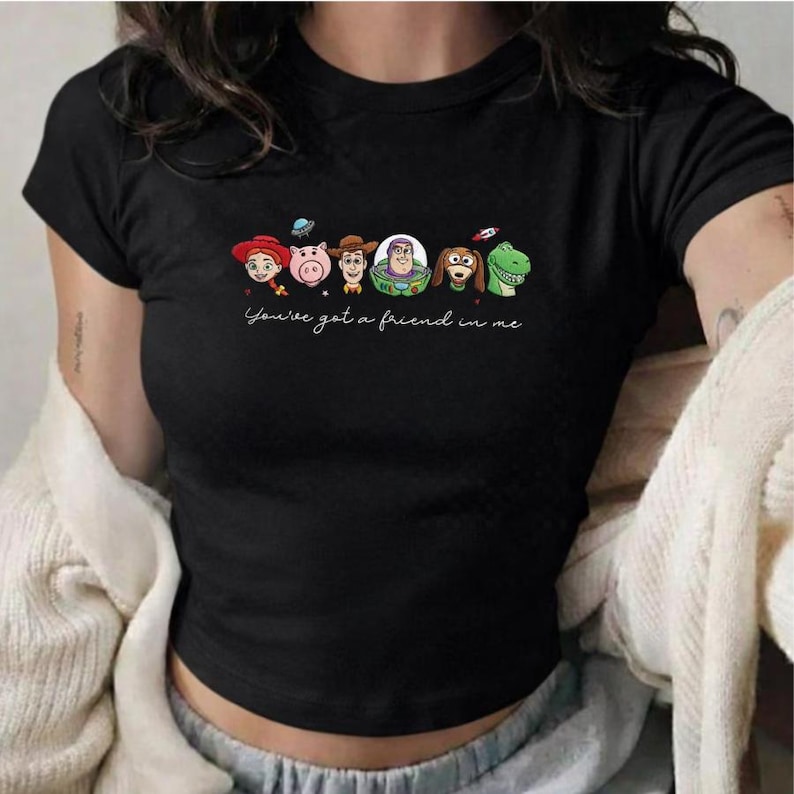 Peut inclure: T-shirt noir avec une illustration de personnages de Toy Story, dont Woody, Hamm, Buzz l'&Eacute;clair et Rex. La phrase "You've got a friend in me" est &eacute;crite en cursive en dessous des personnages.
