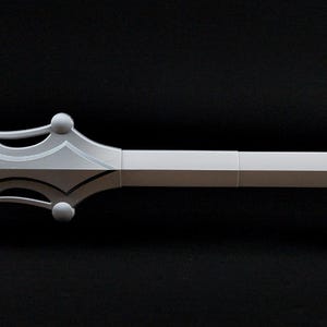 May include: A sword with a long white blade and a pointed tip. The hilt features a white crossguard with four circular accents and a brown, textured grip. The sword is positioned horizontally and is supported by two small black stands.