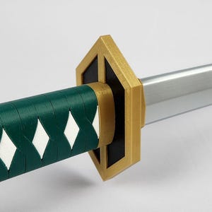 May include: Close-up of a sword with a green and white handle. The handle has a diamond pattern. The guard is gold and black. The blade is silver.