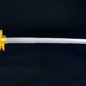 May include: A katana sword with a blue and yellow handle and a silver blade. The sword is displayed on two black stands against a dark background. The handle has a diamond pattern.
